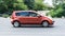 Side view rolling shot with Nissan Note subcompact car. Fast moving orange small hatchback with motion blur effect