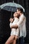 side view of romantic couple in white shirts standing under umbrella under raindrops