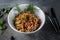 Side view salad of vegetables, olives and shrimp sprinkled with sesame seeds on white plate, grey background in rustic style with