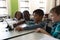 Side view of schoolkids studying on digital tablet while sitting at desk in classroom