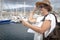 Side view of a senior attractive woman white dressed with backpack. A tablet in the hand. Boats and harbour on background