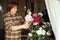 Side view of senior concentrated woman with dark hair spraying bouquet of pink, white roses, setting flowers right.