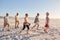 Side View Of Senior Friends Walking Along Sandy Beach On Summer Group Vacation