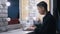 Side view of serious busy young businessman typing on laptop keyboard sitting at mirror with lights in bedroom