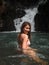 Side view of sexy asian woman in bikini standing in tropical waterfall.