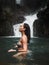 Side view of sexy asian woman in bikini standing in tropical waterfall.