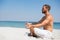 Side view of shirtless man meditating at beach