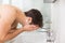 Side view of shirtless man washing face in bathroom