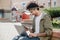 Side view shot of a handsome man using smartphone while working on laptop outdoor, happy guy with african dreadlocks hairstyle