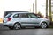 Side view of silver shiny luxurious car parked on empty paved road at low iron fence on background of small red mini vehicle and