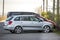 Side view of silver shiny luxurious car parked on empty paved road at low iron fence on background of small red mini vehicle and