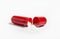 Side view of single red color gel capsule opened, white crystal like powder spilled out, isolated on white background.