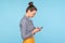 Side view of slightly hunched woman with hair bun using mobile phone with serious unhappy expression, addicted to smartphone