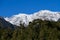 Side view of slightly snow covered mountain peaks with blue cloudless sky in early winter and trees in front