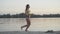 Side view of slim athletic Caucasian woman running along sandy beach at sunset. Wide shot portrait of confident brunette