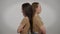 Side view slim young beautiful women standing back to back at grey background. Argued identical twin sisters with