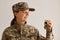 Side view of smiling female soldier wearing military costume, posing indoor in light room, standing with key in hands, buying new