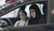 Side view of smiling slim beautiful woman in hijab sitting in car with blurred cute girl on passenger seat at background