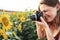 Side view of smiling young woman photographing sunflower using camera in farm on sunny day