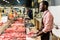 side view of smilng african american male butcher in apron cutting raw meat
