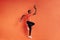 Side view of sportsman jumping in the air with basket ball in hand. Male in sportswear exercising indoors at an orange wall