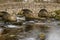 A side view of the stone Pack Horse bridge over the East Dart River in Dartmoor National Park, England