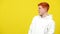 Side view of surprised redhead man standing on the right at yellow background looking away grimacing. Portrait of