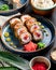 side view of sushi roll with crab and tuna on a plate with ginger and wasabi on wooden background