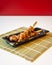 Side view of take away Japanese yakitori skewers on a bamboo mat on white table and red background, with copy space