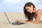 Side view of a teenager girl browsing her laptop lying on the sand of the beach