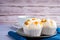 Side view of Thai steamed cupcakes topped with dry fruit on a plate on blue cloth and a cup of white coffee with a wooden