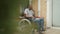 Side view of thoughtful sad disabled African American man in wheelchair on porch in backyard garden. Wide shot of adult