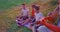 Side view of three boys sitting on yoga mat on ground, old man with gray hair playing guitar. Kids hiking together