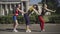 Side view of three cheerful 1980s women in colorful outfit dancing to disco music outdoors. Wide shot of positive slim