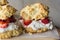 Side view of three strawberry shortcakes with fresh whipped cream on parchment paper.