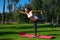 Side view to a happy smiling woman standing in yoga position on a geen grass in the park