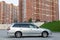 Side view of Toyota Caldina car of 2000 release in the back of a silver T210 station wagon in a parking lot with a green lawn