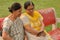 Side view of two Senior Indian woman working on mobile phone/tablet, experimenting with technology on a red park bench in an