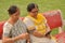 Side view of two Senior Indian woman working on mobile phone/tablet, experimenting with technology on a red park bench in an