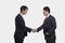 Side view of two smiling businessmen shaking hands, studio shot