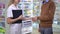Side view unrecognizable pharmacist and client passing shopping bag shaking hands standing in drugstore. Positive