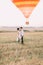 The side view of the vintage dressed newlyweds hugging at the background of the flying colourful airballoon. The field