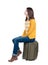 Side view of walking woman in cardigan sits on a suitcase.