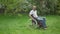 Side view wide shot of confident African American impaired man riding wheelchair in summer garden outdoors. Serious