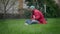 Side view wide shot of happy relaxed African American man sitting on green grass in summer garden with book thinking