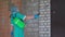 Side view of woman in protective suit disinfecting the exterior wall of the building. Preventive medical treatment of