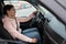 Side view of woman taxi driver sitting in transport, holding steering wheel and looking on road