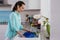 Side view on woman in the turquoise shirt in the interior of the kitchen at the sink washing dish blue in the soft light from the