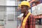 Side view of young African worker man wearing safety vest and helmet, standing at warehouse factory. Male cargo logistics staff