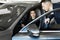 Side view of young beautiful woman sitting inside car and holding hand on steering wheel. She smiling and talking with